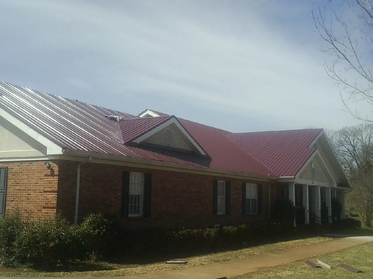 Red metal roof with gabled entries on a long brick building, from a Hail Damage Roof Repair job in Dayton